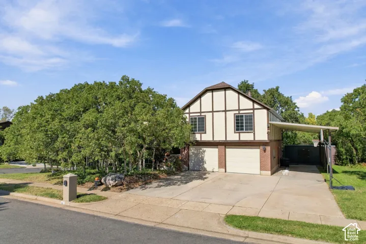 Tudor-style exterior with brick and stucco detailing, featuring a two-car garage, an additional covered carport, and a concrete driveway
