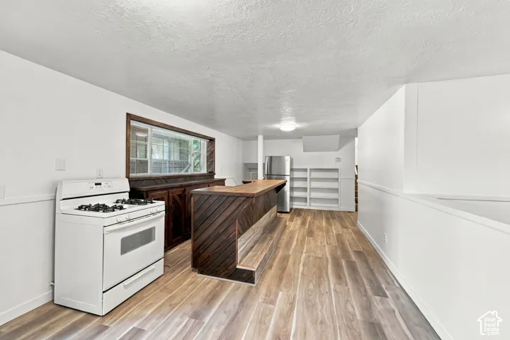 Wood-finish flooring throughout, featuring a built-in wooden bar with a light-toned countertop, white built-in shelving, and a stainless steel refrigerator