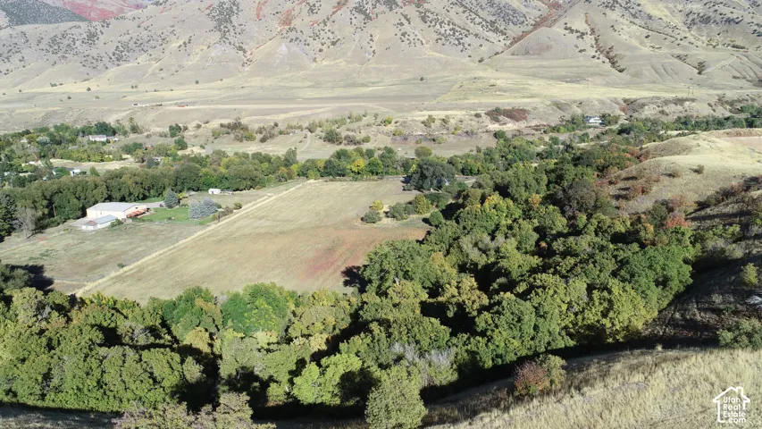 Expansive landscape featuring diverse vegetation, a cultivated field, and distant rolling hills