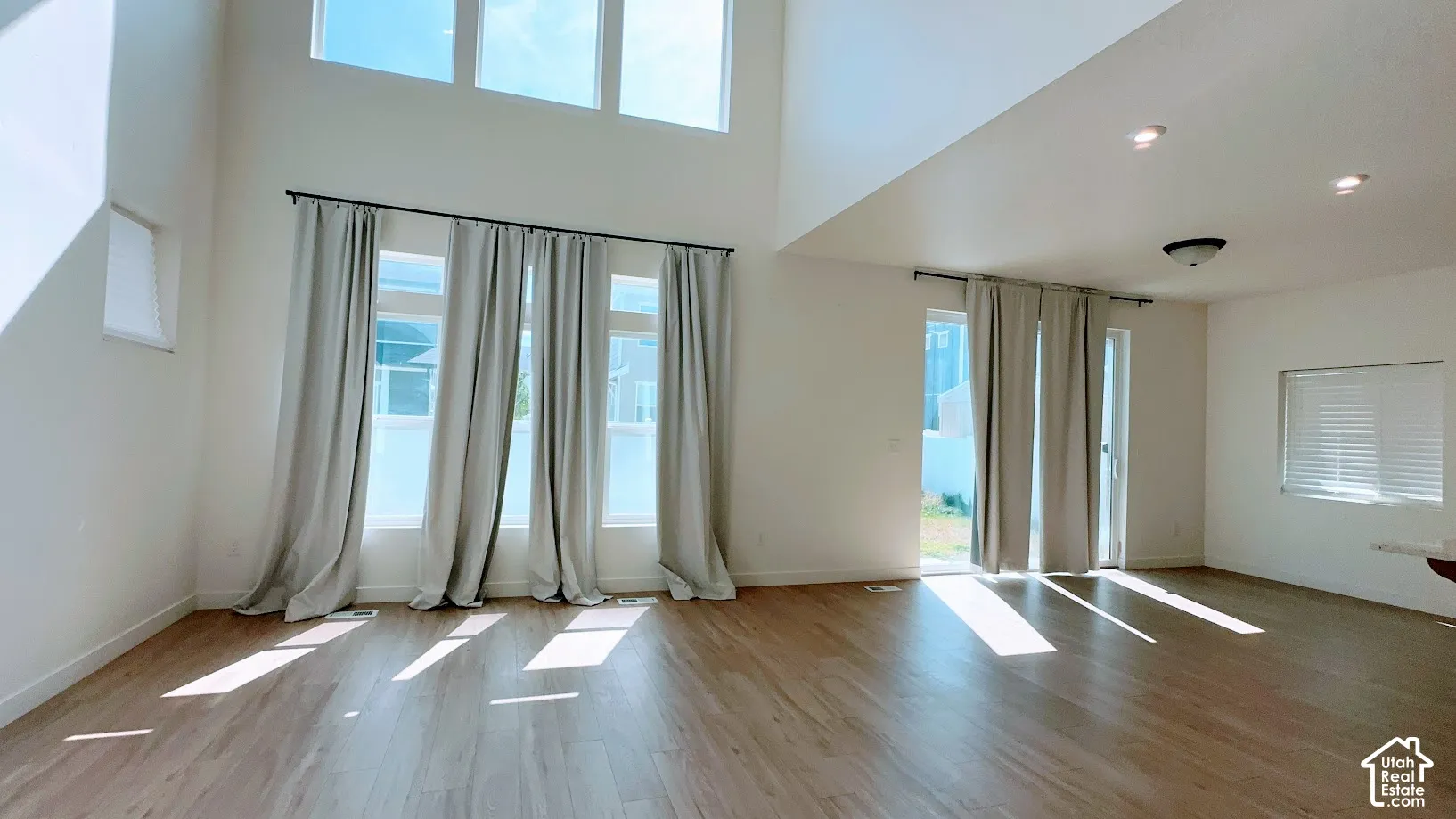 Vaulted ceilings, wood-finish flooring, recessed lighting, and multiple windows with draperies