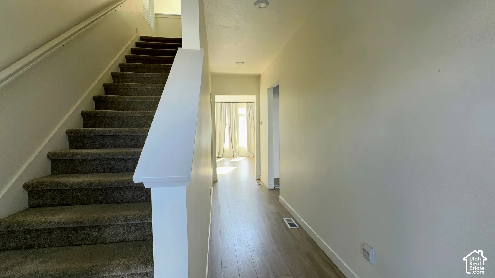 Carpeted staircase with white handrail, wood-finish flooring, recessed lighting, and bright natural light