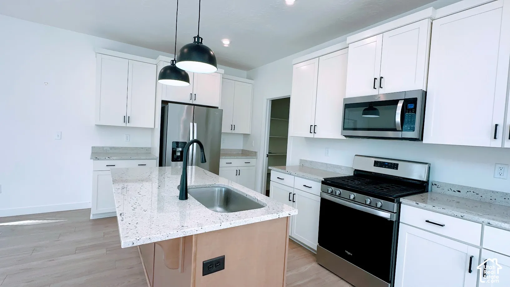 Kitchen featuring a central island with an integrated sink, white cabinetry, stainless steel appliances, and light-toned countertops
