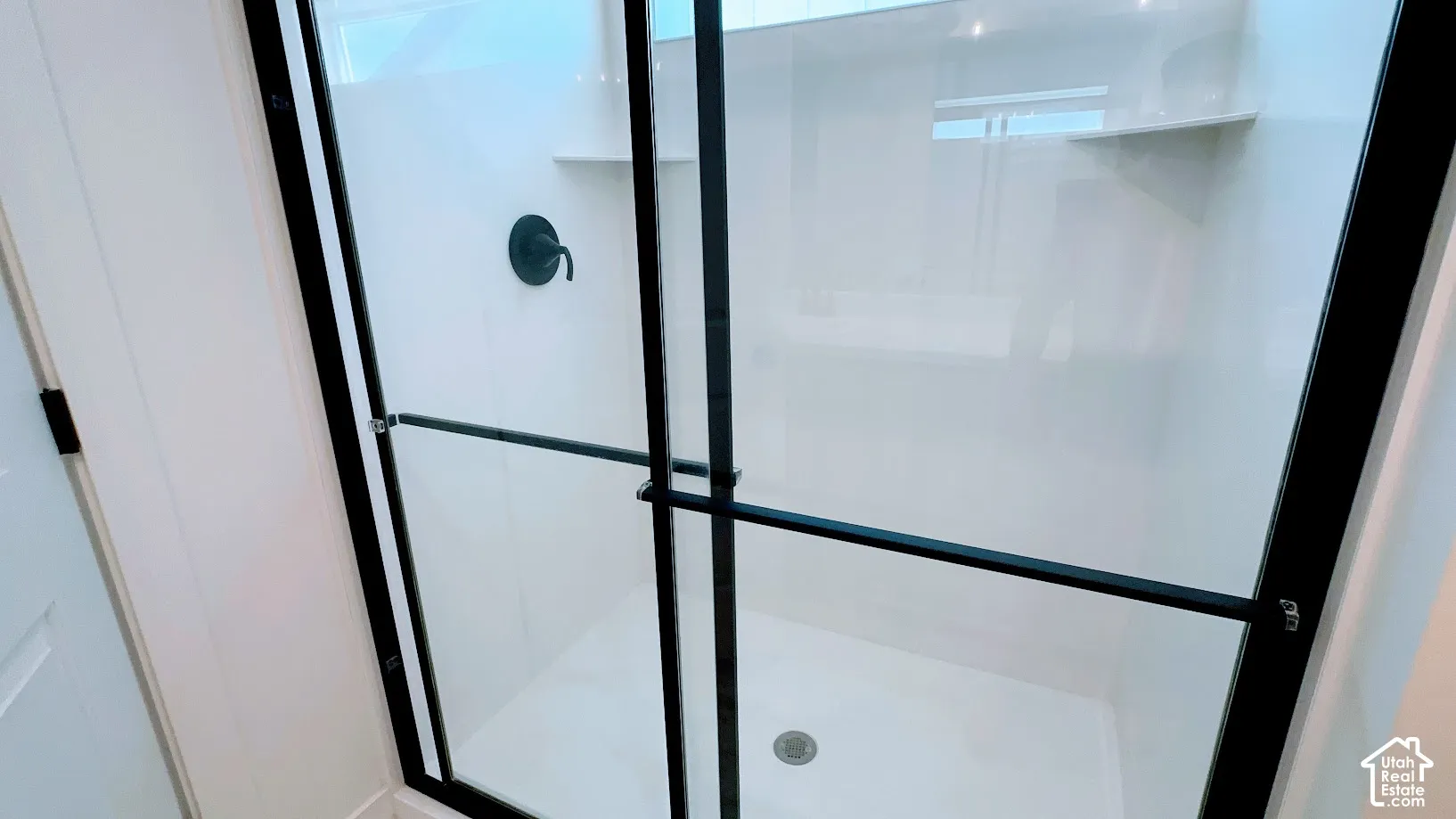 Shower enclosure with black-framed clear glass doors, integrated shelving, and a matte black shower fixture