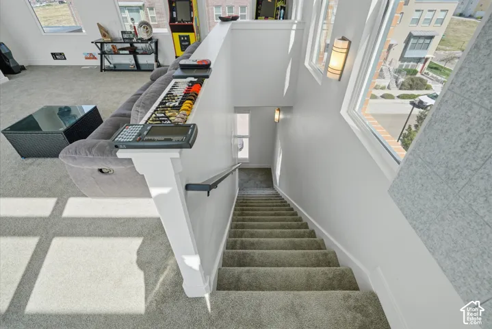 Carpeted staircase with white balustrade and handrail, illuminated by natural light from multi-pane windows and wall-mounted sconces