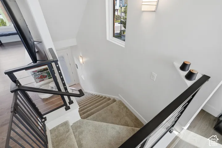 Carpeted staircase with dark metal and cable railing, complemented by wood-finish flooring and a built-in wall sconce