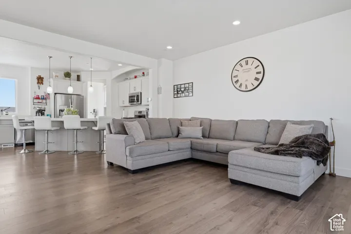 Open-concept living space featuring wood-finish flooring, recessed lighting, a kitchen island with pendant lighting, and stainless steel appliances