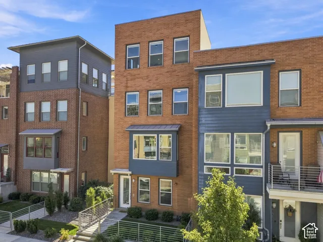 Modern multi-level exterior with brick and paneling accents, large windows, and an upper-level balcony featuring metal railings