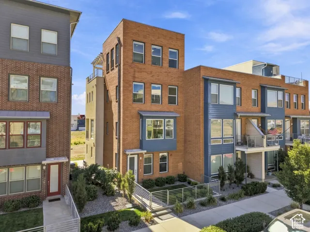 Contemporary multi-story exterior with brick and siding accents, multiple balconies, and a flat roof with a visible rooftop terrace