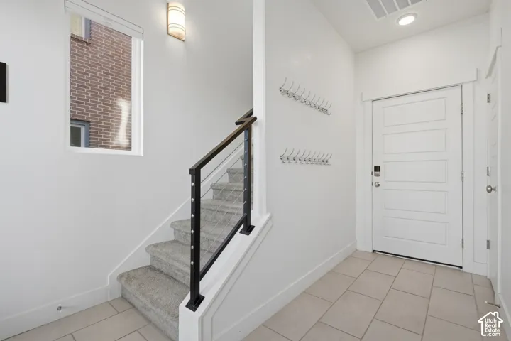 Entryway featuring tiled flooring, a contemporary staircase with metal railing, a window, and a paneled entry door