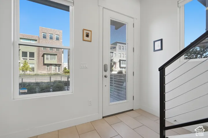 White interior walls with a full-light entry door, a window with a roller shade, and light-toned tile flooring