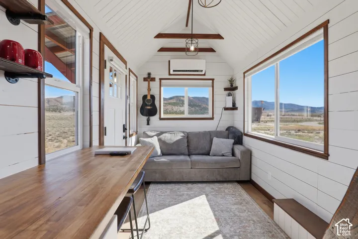 Vaulted ceiling featuring exposed wood beams, wood-finish flooring, white shiplap walls, multiple windows, and a built-in wood countertop