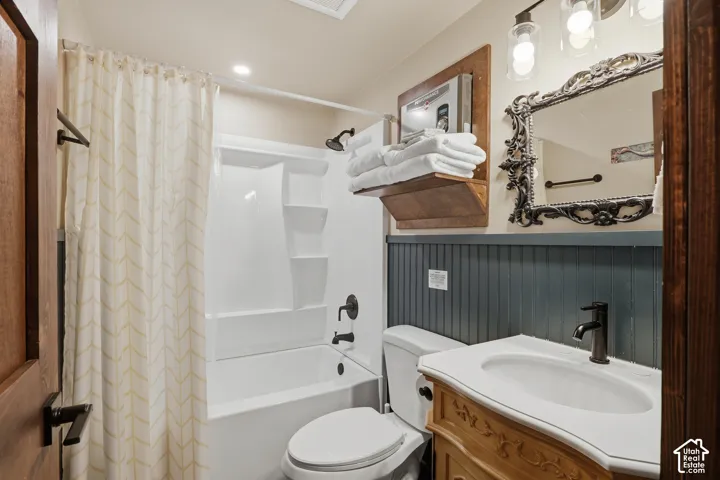 Bathroom featuring a built-in tub with shower, beadboard wainscoting, a vanity with an integrated sink, and an ornate framed mirror
