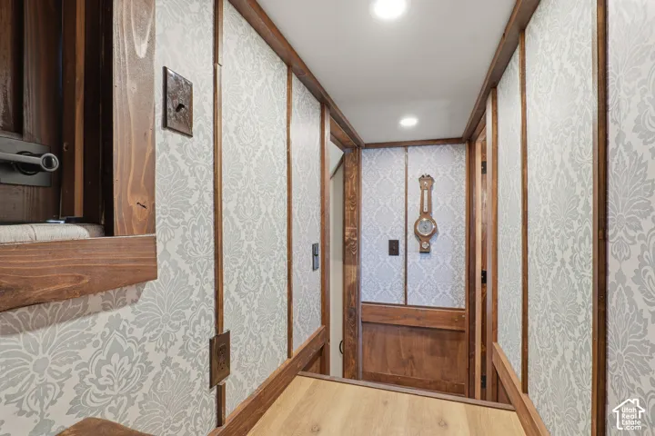 Recessed ceiling lighting illuminates a hallway featuring wood-finish flooring, wood paneling, and patterned wall coverings