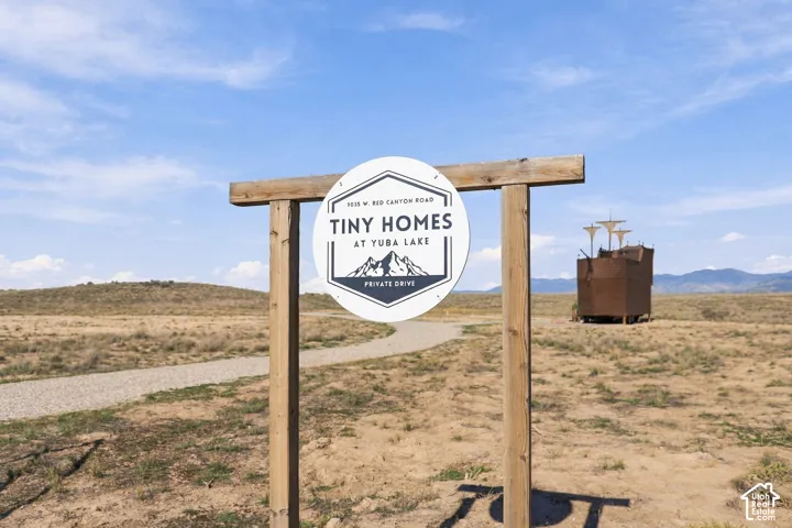Prominent wooden signage with a circular display, gravel pathway, expansive arid landscape, and distant mountains