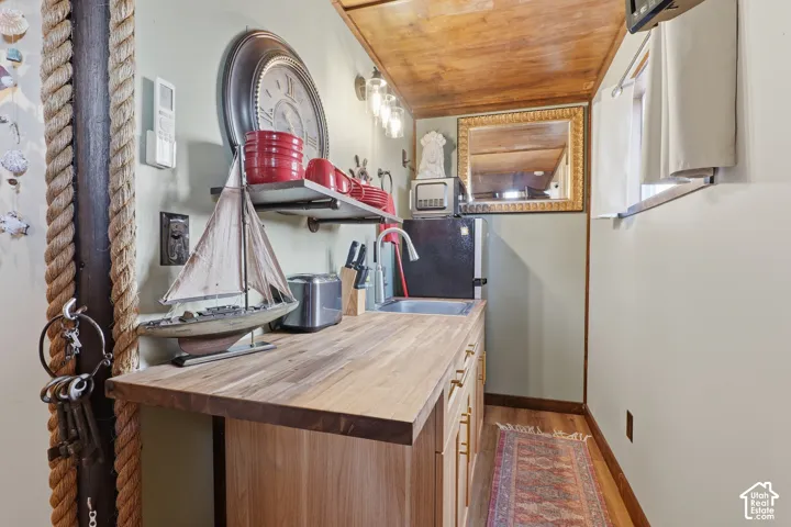 Compact kitchen area featuring wood-finish countertops, light wood-finish cabinetry with gold-tone hardware, a stainless steel sink with a gooseneck faucet, and open shelving