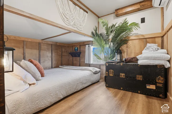 Wood-finish flooring with paneled walls, exposed wood beams, and a window for natural light