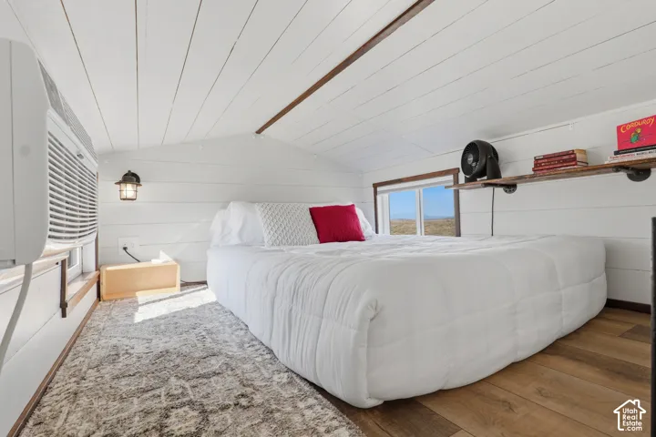 Loft space featuring white shiplap walls and ceiling, wood-finish flooring, a window-mounted air conditioning unit, and a wall-mounted light fixture