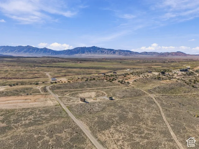 Expansive arid landscape featuring scattered brush, unpaved roads, and distant mountain ranges