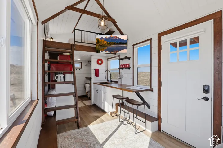 Open-concept interior featuring wood-finish flooring, white shiplap walls, a kitchen with white cabinetry, and a loft space with a black metal railing