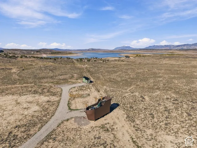 Expansive natural landscape with a prominent body of water in the background, a gravel drive, and unique structures