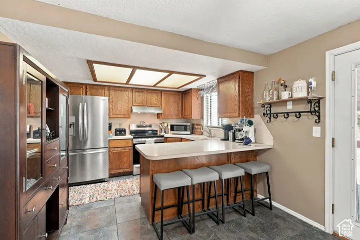 Kitchen featuring wood-finish cabinetry, stainless steel appliances, a breakfast bar, and tile flooring