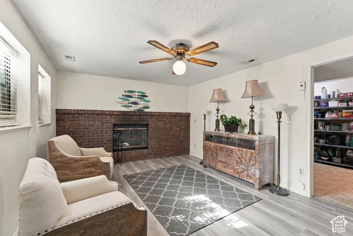 Brick fireplace with a dark metal insert, wood-finish flooring, and a ceiling fan with integrated lighting