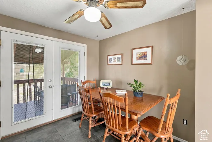 White French doors with clear glass panes, a wood-finish ceiling fan with a central light fixture, and dark grey floor tiles