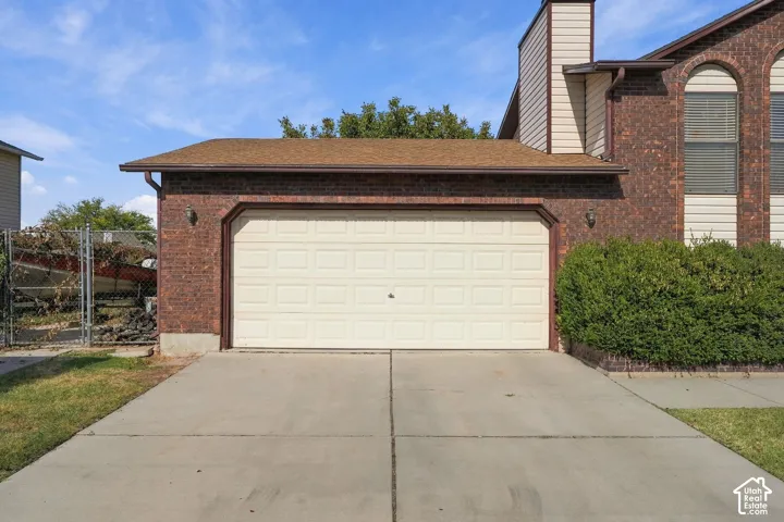 Brick exterior with a two-car garage, concrete driveway, and mature landscaping