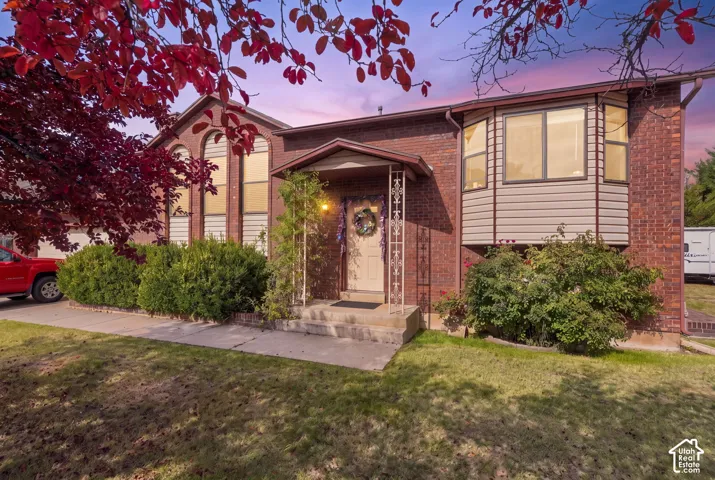 Brick exterior with a covered entry, arched windows, a bay window with horizontal siding, and established landscaping