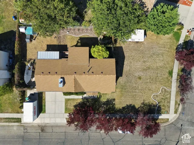 Aerial view showcasing a brick residence with a spacious yard featuring mature landscaping, including ornamental trees and shrubs