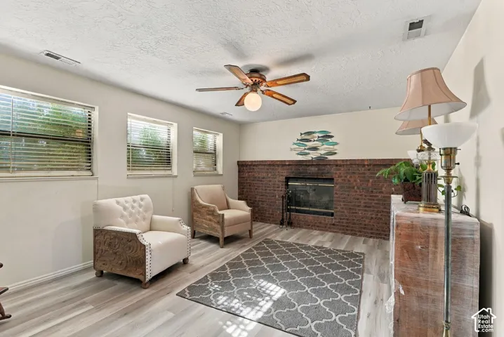 Brick-faced fireplace with a dark metal insert, light wood-finish flooring, and multiple windows