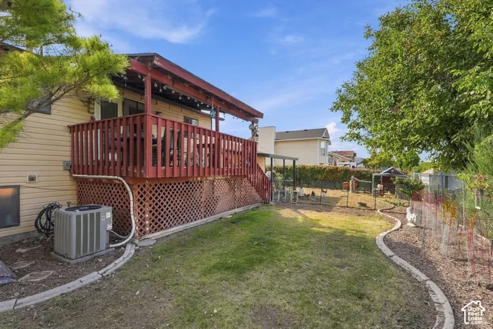 Expansive backyard with a covered wooden deck, lattice skirting, manicured lawn, and defined landscaping beds