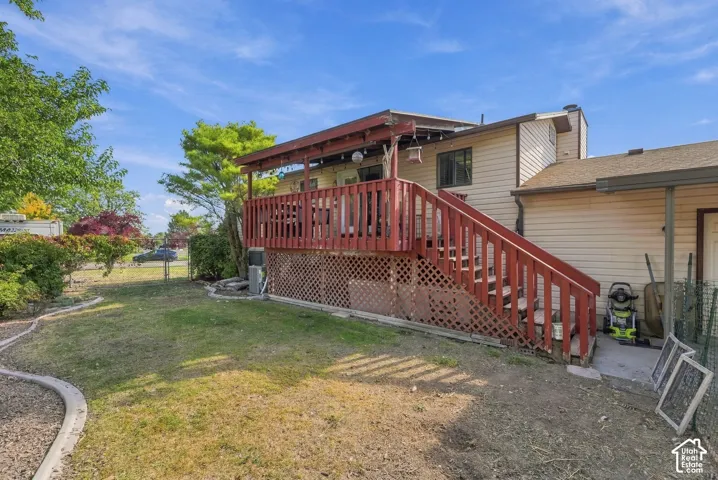 Expansive backyard featuring a large wooden deck with railing and stairs, mature landscaping, and a chain-link fence