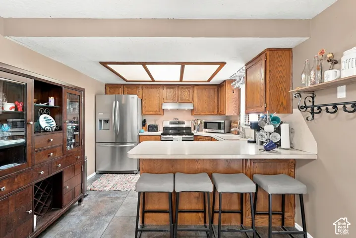 Kitchen featuring wood cabinetry, stainless steel appliances, a breakfast bar, and tile flooring