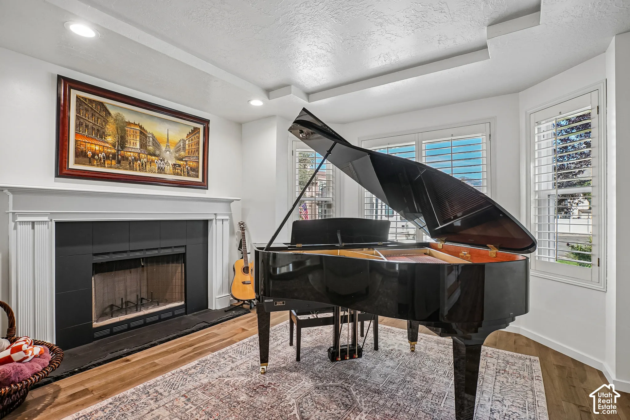 Hardwood-finish flooring, recessed lighting, white fireplace mantel, black fireplace surround, and bay windows with white plantation shutters