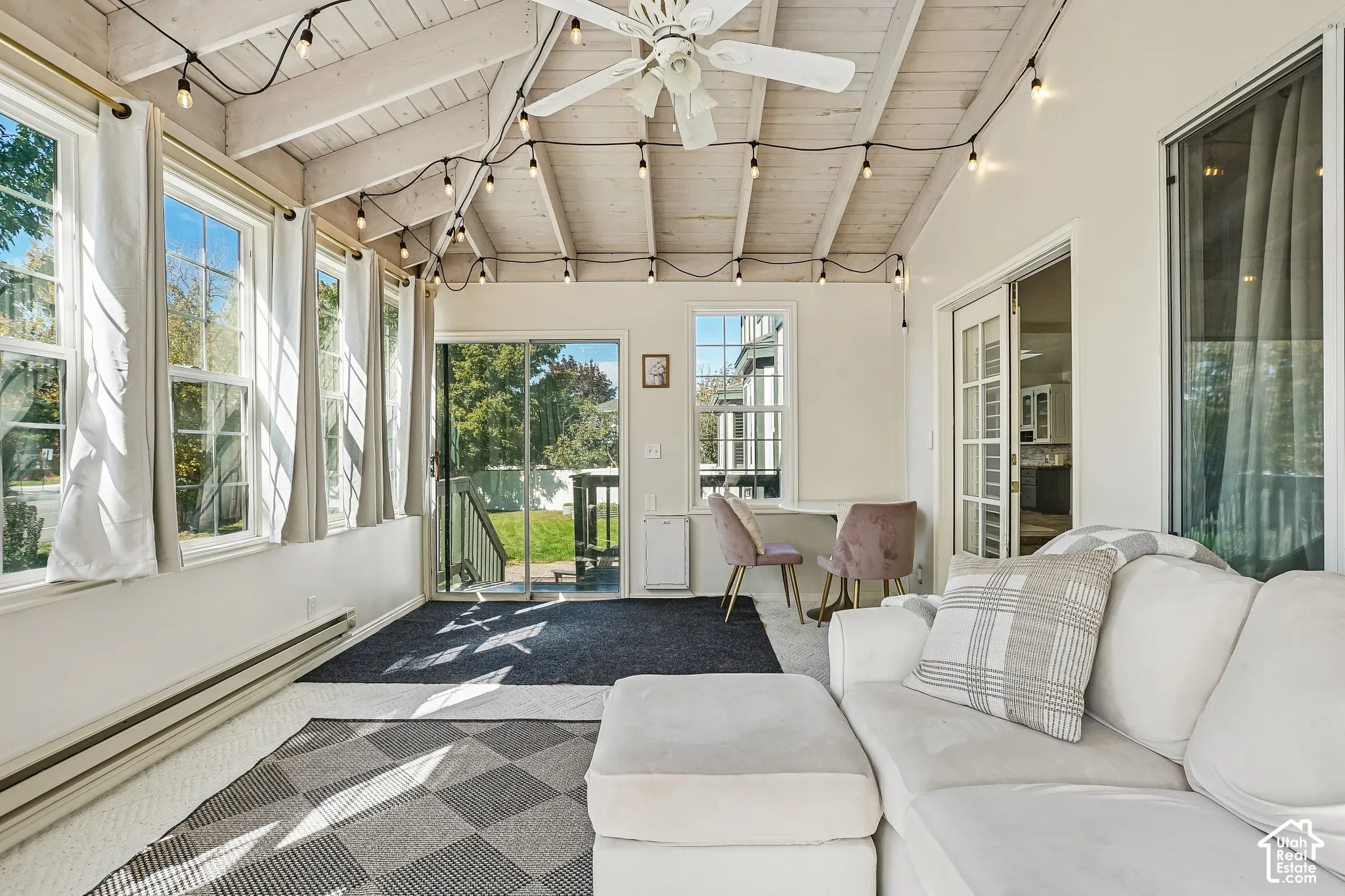 Sunroom with exposed beam ceiling, multiple windows, double sliding glass doors, and a ceiling fan