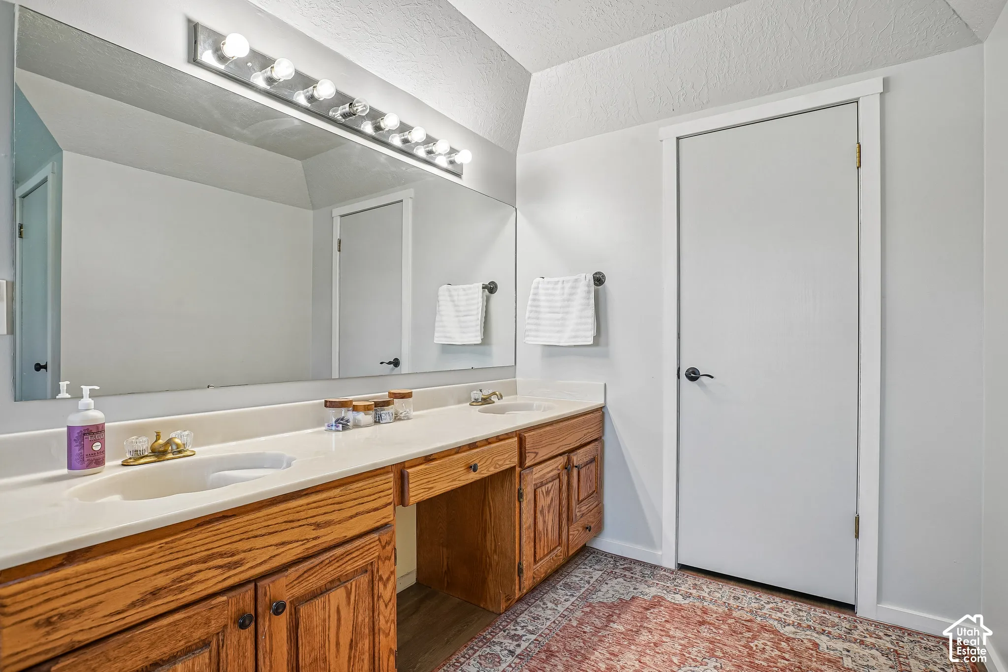 Dual vanity with integrated sinks, wood-finish cabinetry, and a full-width mirror with overhead lighting