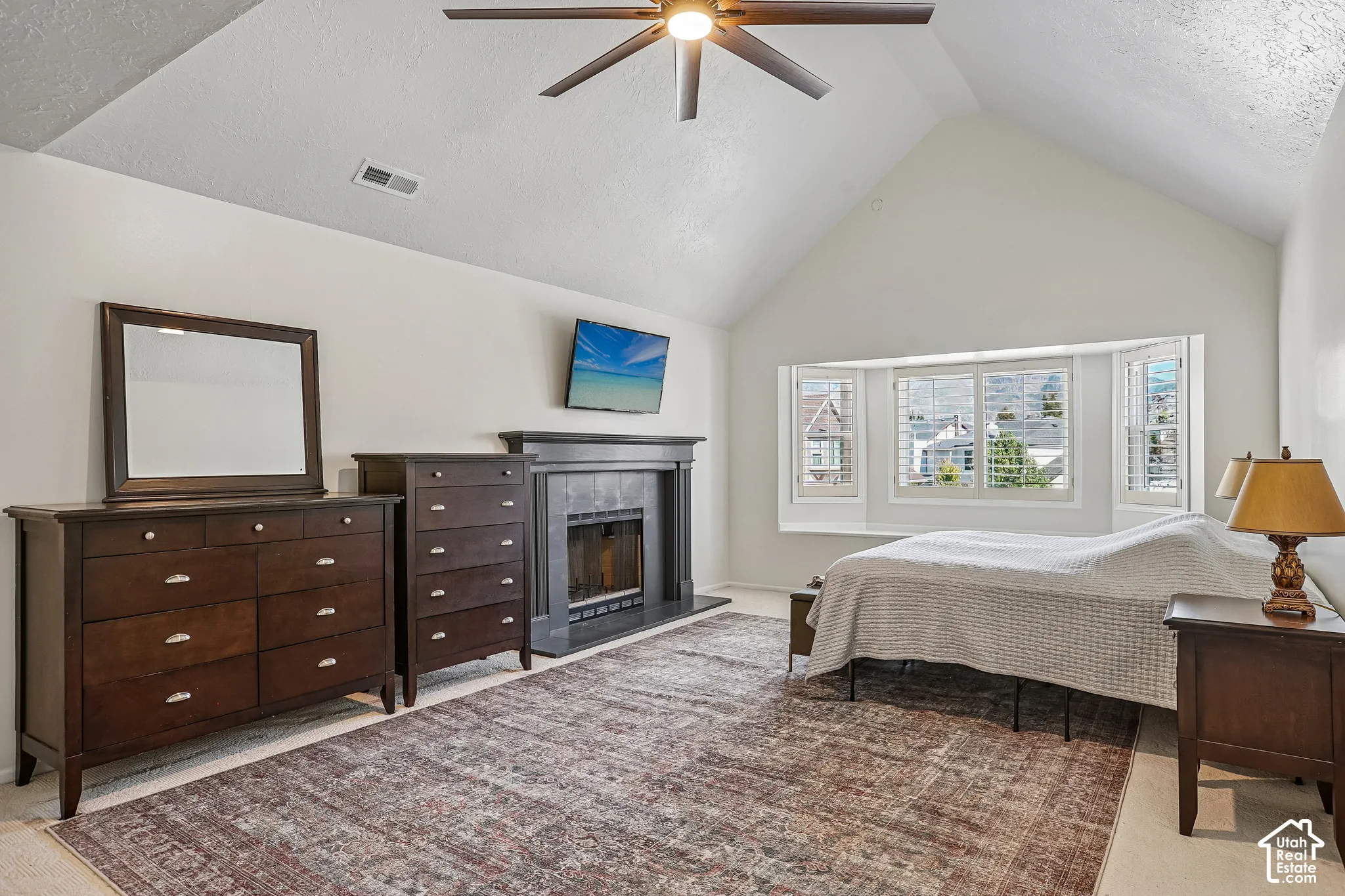 Vaulted ceiling with ceiling fan, bay window with integrated bench, built-in fireplace, and light-colored wall-to-wall carpeting