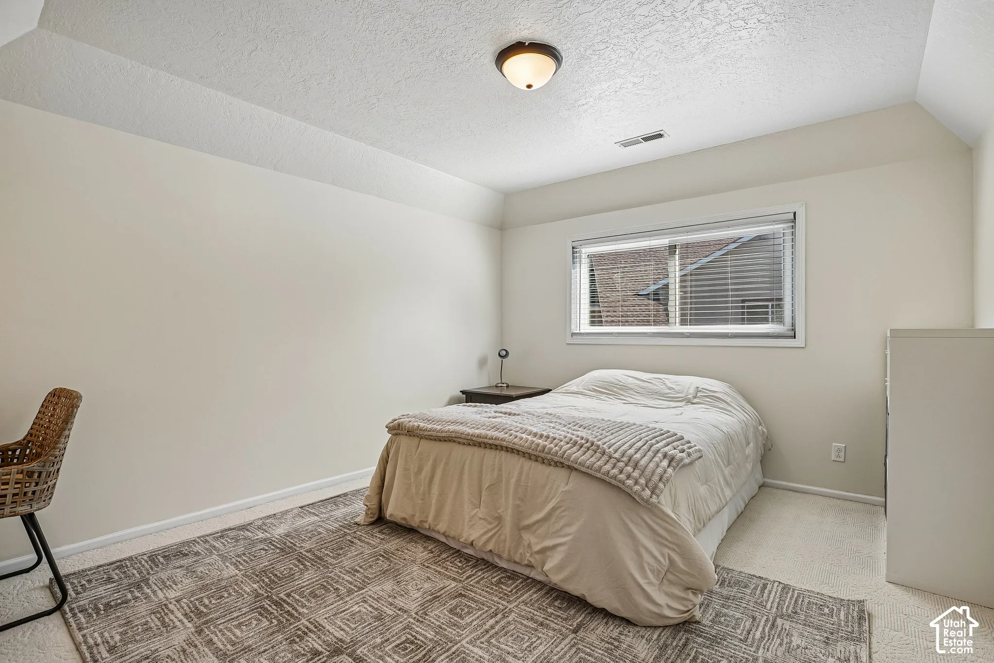 Carpeted flooring, vaulted ceiling, single window, flush mount lighting, and neutral wall tones