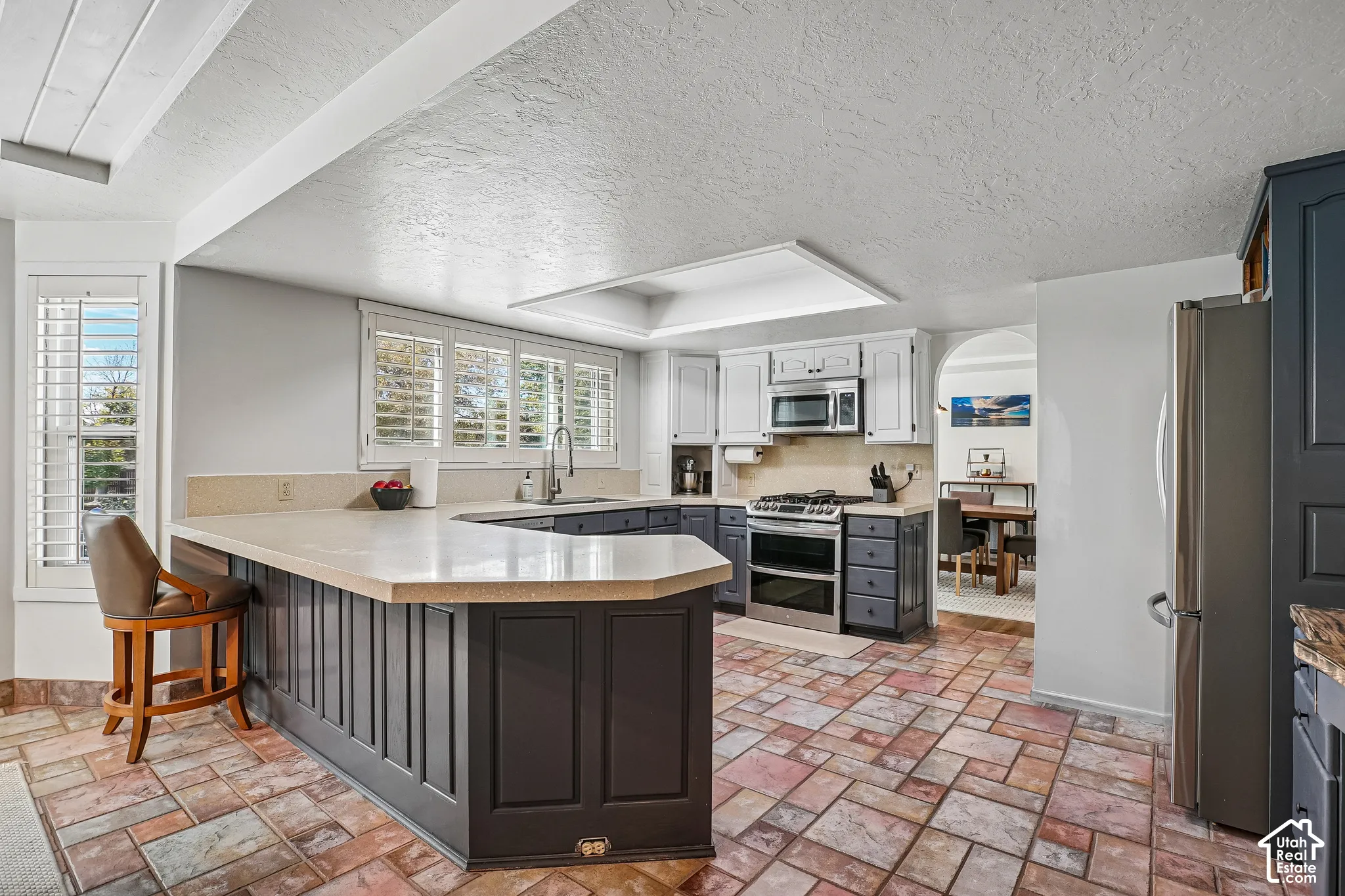 Kitchen featuring a large island with paneling, stone-finish countertops, stainless steel appliances, and a tiled floor