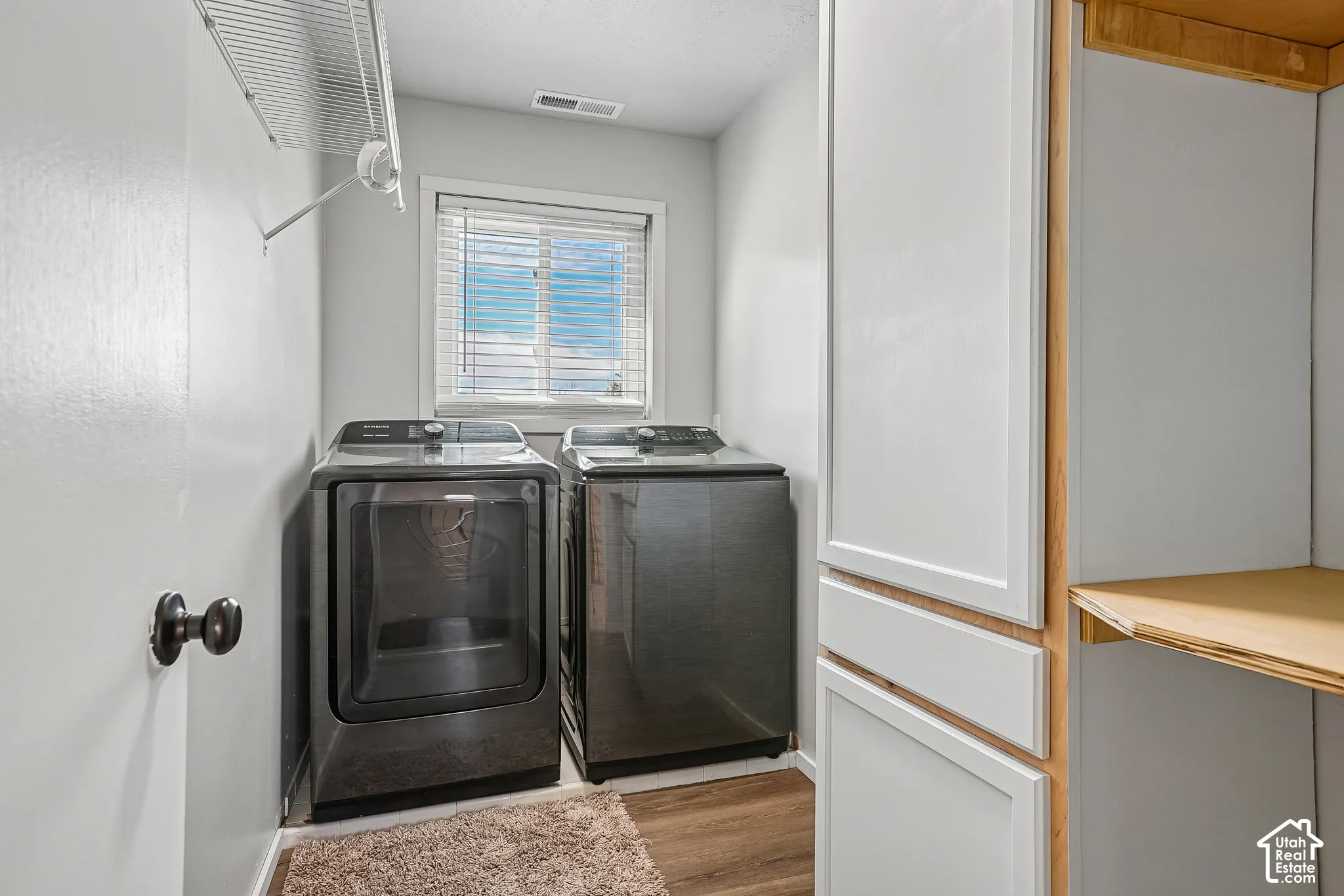 Laundry area featuring wood-finish flooring, a window with blinds, and built-in white cabinetry with wood trim