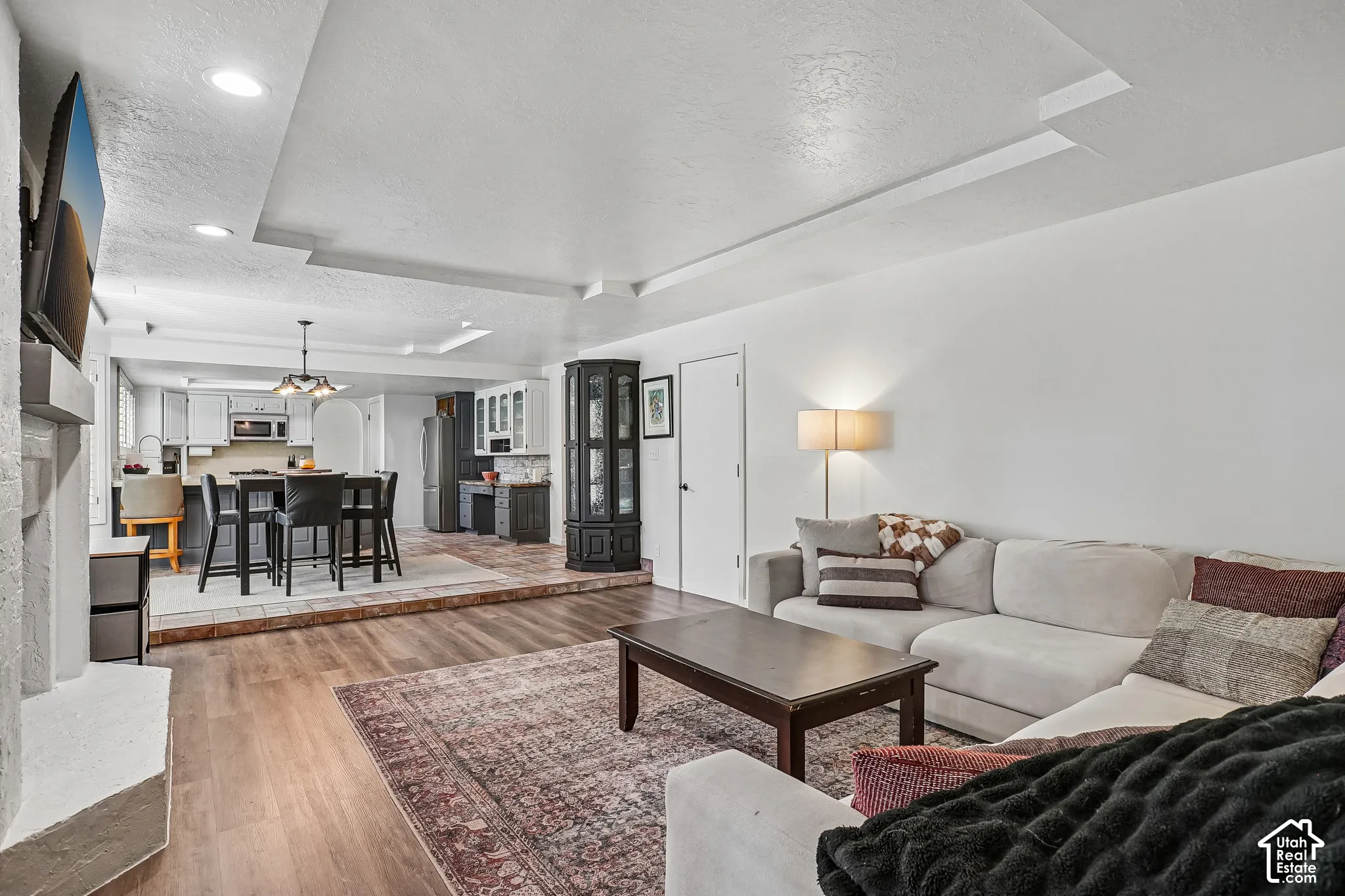 Wood-finish flooring with a raised tile dining area, recessed lighting, and a white fireplace surround