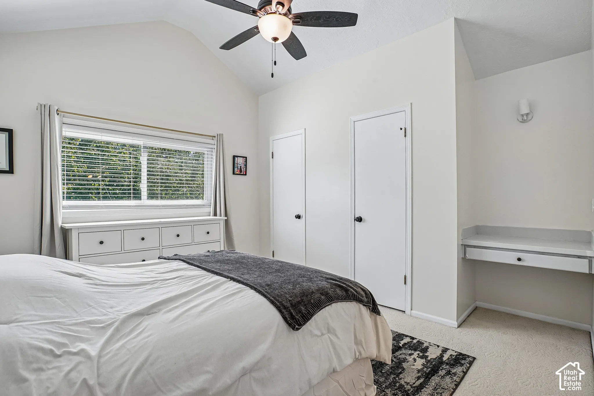 Vaulted ceiling with a ceiling fan, dual white closet doors, built-in desk with a single drawer, and a window with blinds