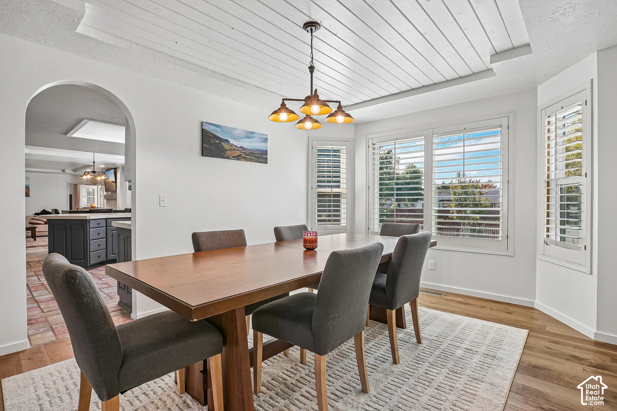 Dining area featuring a shiplap ceiling, a multi-light chandelier, a bay window with plantation shutters, wood-finish flooring, and an arched entryway