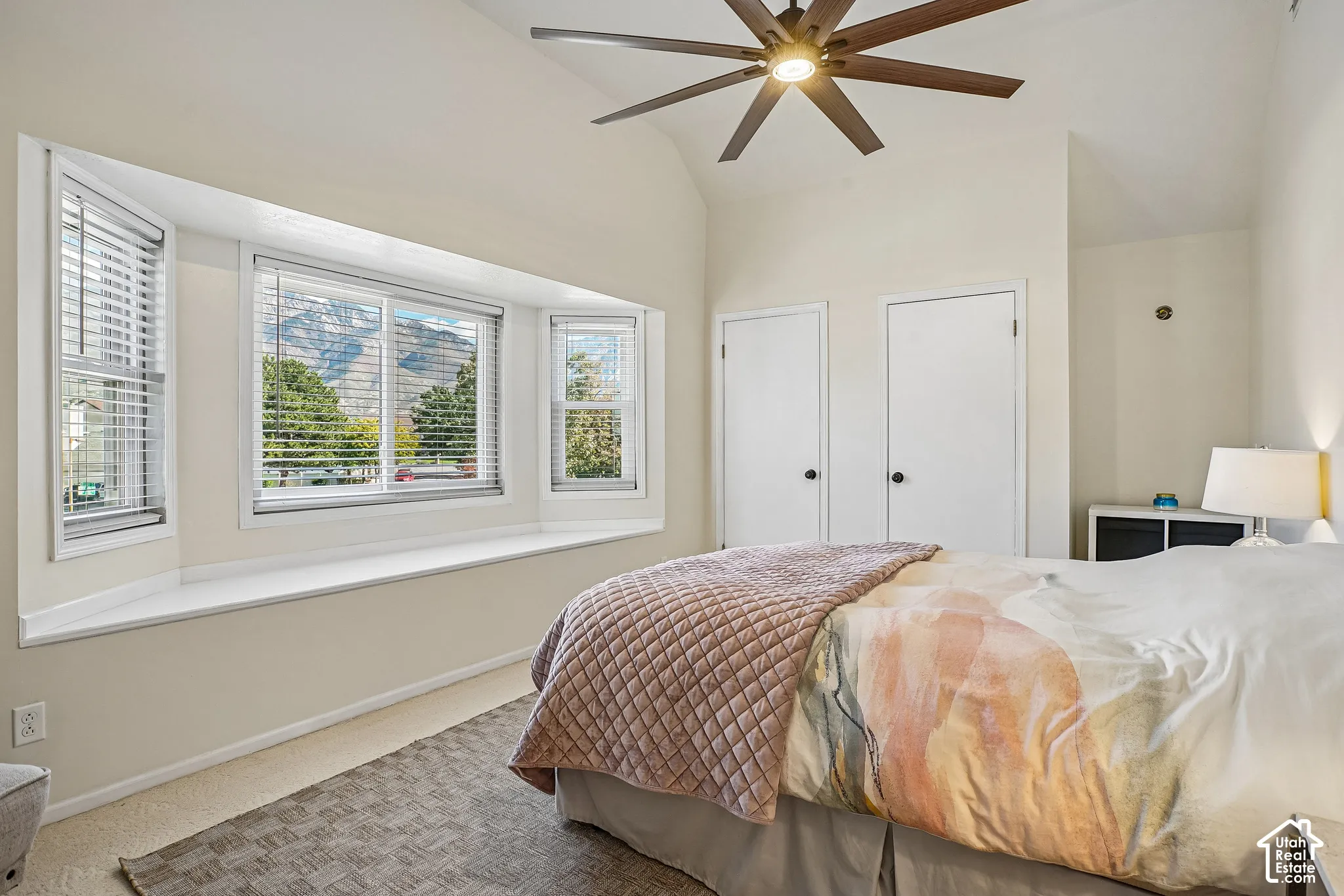 Vaulted ceiling with an attached ceiling fan, bay window with integrated seating, two white paneled doors, and wall sconce lighting