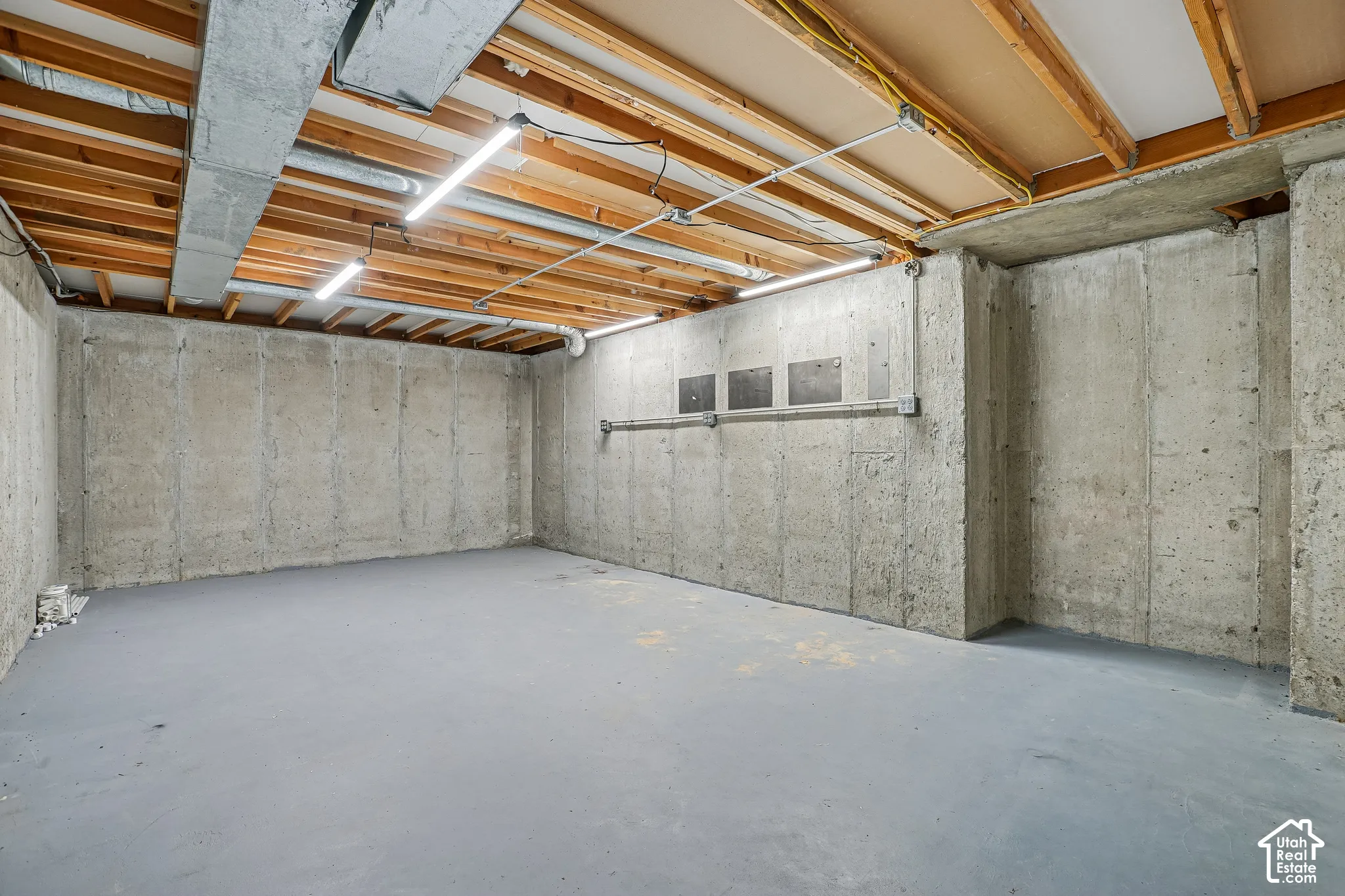 Concrete walls with exposed wood joist ceiling and overhead lighting