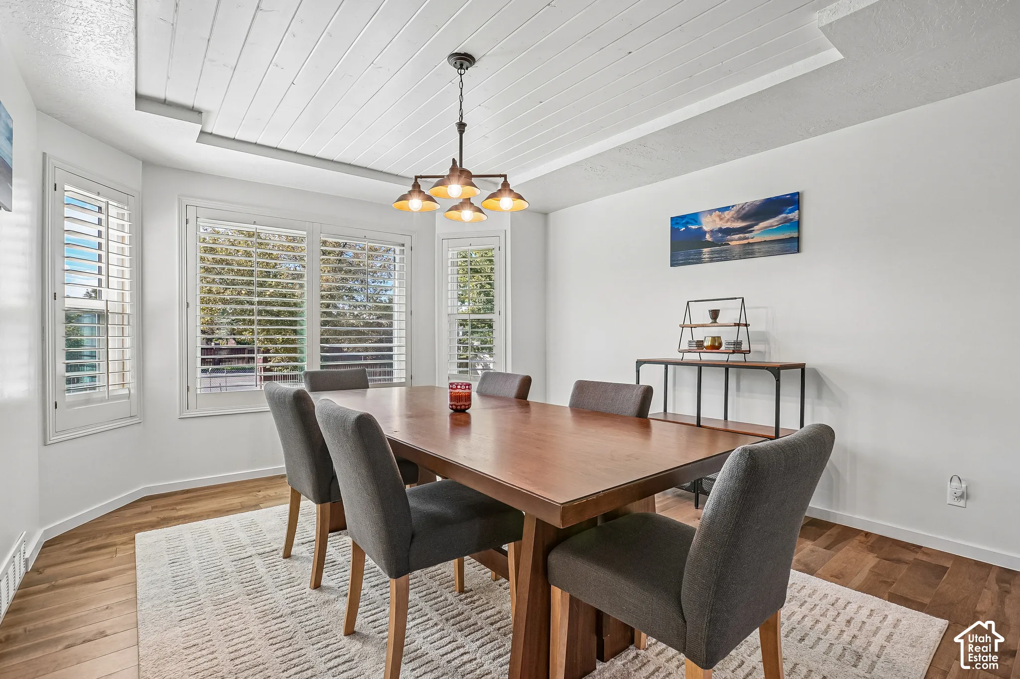 White shiplap ceiling, wood-finish flooring, bay window with plantation shutters, pendant lighting fixture, and white painted walls