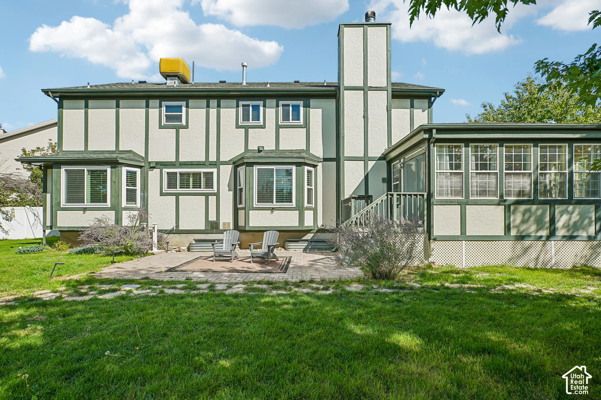 Exterior featuring bay windows, a sunroom extension, a prominent chimney, and a stone patio