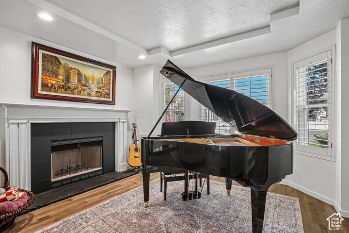 Hardwood-finish flooring, recessed lighting, white fireplace mantel, black fireplace surround, and bay windows with white plantation shutters