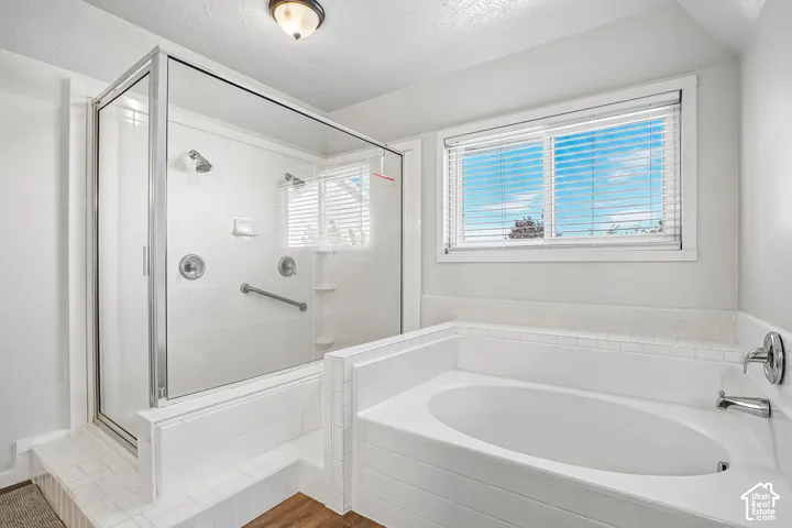 White tiled soaking tub, separate glass-enclosed shower, chrome fixtures, and a window with blinds